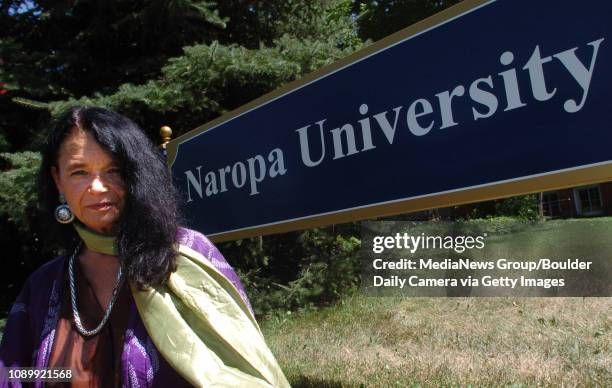 Anne Waldman in purple and green,
sitting in front of the sign
for Naropa University
